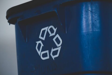 A white recycling symbol on the side of a blue plastic bin
