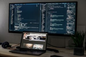 A laptop and a wide monitor displaying lines of code on a desk