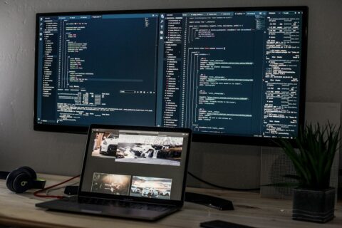 A laptop and a wide monitor displaying lines of code on a desk